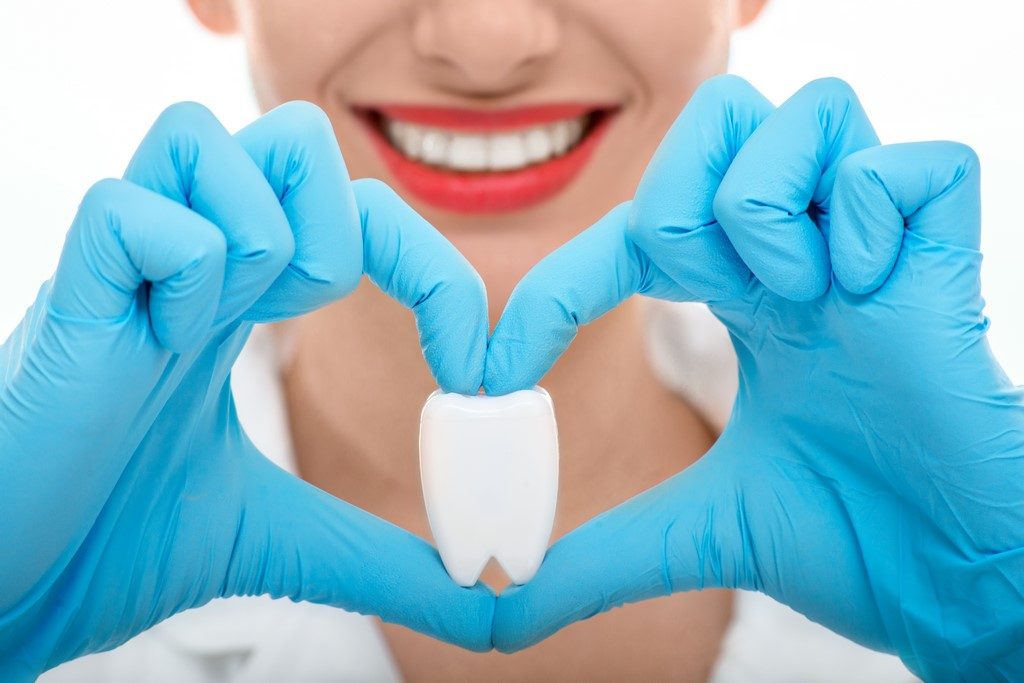 retrato de una joven dentista sujentando un diente con los dedos de su mano y formando un corazón